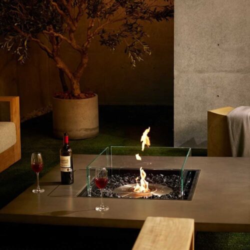 Vertigo 50 Fire Pit Table in a modern outdoor lounge with a central flame and glass wind guard.